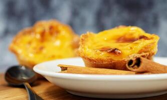 drei Pastell- de nata oder Portugiesisch Ei Torte und Zimt Stöcke auf ein hölzern braun Hintergrund. Pastell- de belem ist ein klein Nachtisch, ein becherförmig Gebäck gemacht von Puff Gebäck mit Pudding. foto