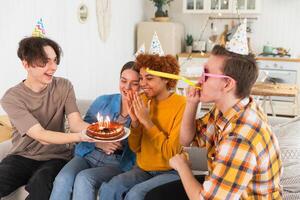 machen ein Wunsch. Frau tragen Party Deckel weht aus Verbrennung Kerzen auf Geburtstag Kuchen. glücklich Geburtstag Party. Gruppe von freunde wünscht sich Mädchen glücklich Geburtstag. Menschen feiern Geburtstag mit Party beim Zuhause foto