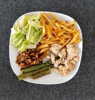 hausgemacht gegrillt Hähnchen mit Französisch Fritten, Spargel, gegrillt gehackt Aubergine und Grün Salat, serviert auf ein Weiß Teller foto