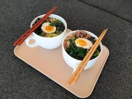 asiatisch Ramen Soba Nudel Suppe schließen oben mit Huhn, gekocht Ei, nori, Grün Spinat und Grün Zwiebel serviert mit Essstäbchen foto