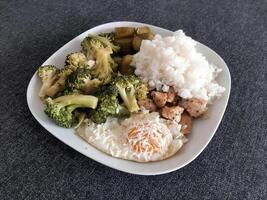 hausgemacht Gericht mit Brokkoli, gebraten Eier mit Käse, Hähnchen gebacken Fleisch, Reis und Gurken serviert auf Weiß Teller foto
