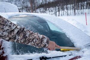 hand mit bürste, die schnee auf der windschutzscheibe des autos fegt foto