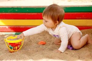 Baby Mädchen spielen im das Sandkasten auf das Spielplatz auf ein Sommer- sonnig Tag foto