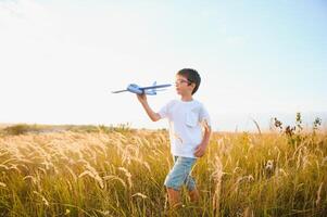 das Kind läuft mit ein Spielzeug Ebene. Sohn Träume von fliegend. glücklich Kind, Junge, läuft auf das Sonne spielen mit ein Spielzeug Flugzeug auf das Sommer- Feld foto