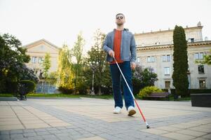 jung blind Mann mit Weiß Stock Gehen über das Straße im Stadt foto