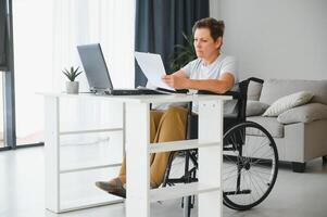 Mitte Alter Frau mit Laptop Sitzung auf Rollstuhl beim Zuhause foto