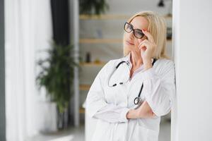 weiblich Arzt tragen Labor Mantel und Stethoskop und halten Zwischenablage im ihr Hände während Stehen beim Krankenhaus. foto