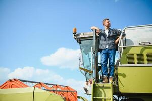 Mähdrescher Maschine Treiber Klettern in ein Taxi zu Ernte seine Weizen Feld. Farmer bekommen im kombinieren auf Leiter halten Geländer. Agronom. Rancher nach Ernte Arbeit foto