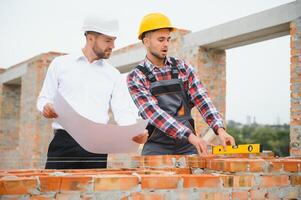 Ingenieur und Baumeister im schwer Hüte diskutieren Entwurf auf Konstruktion Seite? ˅. foto