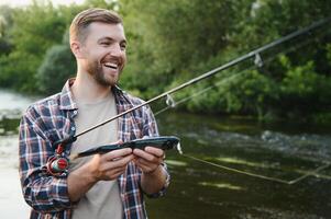 Mann mit Angeln Stange, Fischer Männer im Fluss Wasser draussen. fangen Forelle Fisch im Netz. Sommer- Angeln Hobby foto