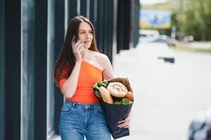 jung Frau Stehen in der Nähe von das Geschäft mit ein Paket von Lebensmittel. foto