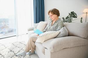 alt Dame Sitzung auf Couch und genießen interessant Roman Lager Foto