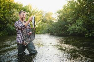 Mann mit Angeln Stange, Fischer Männer im Fluss Wasser draussen. fangen Forelle Fisch im Netz. Sommer- Angeln Hobby foto