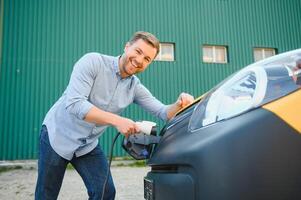 Mann Laden elektrisch Auto durch das Haus foto