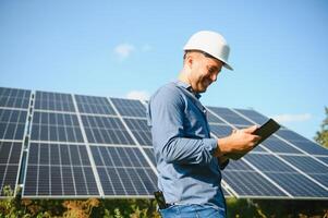 das Porträt von ein jung Ingenieur prüft mit Tablette Betrieb mit Sonne, Sauberkeit auf Feld von Photovoltaik Solar- Tafeln. Konzept verlängerbar Energie, Technologie, Elektrizität, Service, Grün Leistung foto