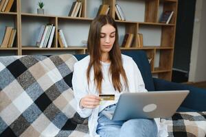 online speichern. glücklich Mädchen tun Einkaufen über Internet mit Laptop und Anerkennung Karte, Sitzung auf Couch, Copyspace foto