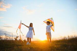 glücklich Kinder starten ein Drachen im das Feld beim Sonnenuntergang. wenig Junge und Mädchen auf Sommer- Urlaub. foto
