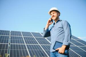 das Porträt von ein jung Ingenieur prüft mit Tablette Betrieb mit Sonne, Sauberkeit auf Feld von Photovoltaik Solar- Tafeln. Konzept verlängerbar Energie, Technologie, Elektrizität, Service, Grün Leistung foto