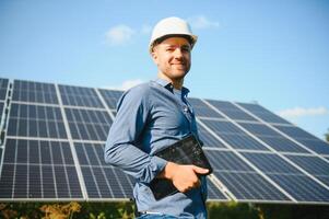 das Porträt von ein jung Ingenieur prüft mit Tablette Betrieb mit Sonne, Sauberkeit auf Feld von Photovoltaik Solar- Tafeln. Konzept verlängerbar Energie, Technologie, Elektrizität, Service, Grün Leistung foto