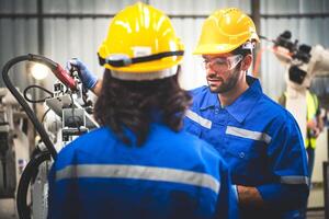 zwei Ingenieure Mechaniker mit Computer Regler Roboter Arm zum Schweißen Stahl im Stahl Fabrik Werkstatt. Industrie Roboter Programmierung Software zum automatisiert Herstellung Technologie . foto