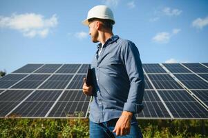 das Porträt von ein jung Ingenieur prüft mit Tablette Betrieb mit Sonne, Sauberkeit auf Feld von Photovoltaik Solar- Tafeln. Konzept verlängerbar Energie, Technologie, Elektrizität, Service, Grün Leistung foto