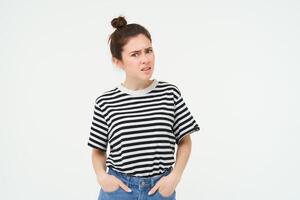 Porträt von verwirrt jung Frau, suchen mit Ungläubigkeit, erziehen ihr Augenbrauen und starren schockiert beim Kamera, Stehen Über Weiß Hintergrund foto