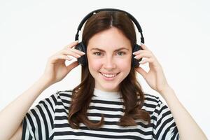 Porträt von schön Frau im kabellos Kopfhörer, Hören Musik, mit Kopfhörer, lächelnd beim Kamera, Stehen Über Weiß Hintergrund foto