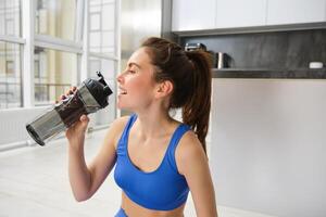 Porträt von Sportlerin Trinken Wasser während trainieren Session im Leben Zimmer, tut ihr Fitness Ausbildung Übungen beim Zuhause foto