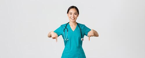 COVID-19, Gesundheitswesen Arbeitskräfte, Pandemie Konzept. lächelnd angenehm asiatisch weiblich Arzt, Therapeut oder Arzt im Peelings mit Stethoskop, zeigen Finger runter, Show Klinik Banner foto