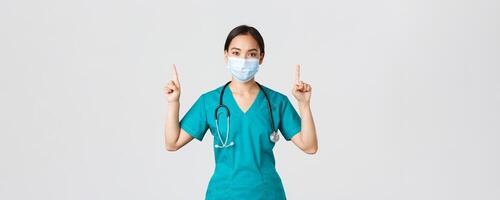 COVID-19, Coronavirus Krankheit, Gesundheitswesen Arbeitskräfte Konzept. jung Fachmann asiatisch weiblich Arzt, Krankenschwester im medizinisch Maske und Peelings, zeigen Finger hoch, zeigen Weg, Werbung foto