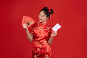 glücklich asiatisch Frau tragen rot Qipao Kleid halten Anerkennung Karte und Angpao oder rot Paket Geld Geschenk isoliert auf rot Hintergrund. foto