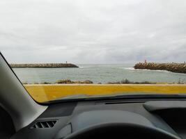 Meer Aussicht von das Auto Innere. Leuchtturm und Ozean Seebrücke durch das Lenkung Rad foto