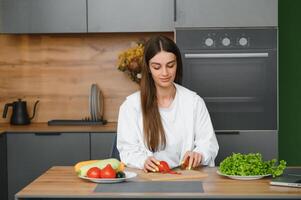 glücklich lächelnd süß Frau ist vorbereiten ein frisch gesund vegan Salat mit viele Gemüse im das Küche beim Zuhause und versuchen ein Neu Rezept foto