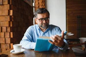 reifen gut aussehend Mann lesen ein Buch im ein Cafe foto