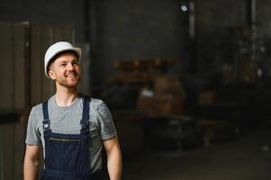 lächelnd und glücklich Mitarbeiter. industriell Arbeiter drinnen im Fabrik. jung Techniker mit Weiß schwer Hut. foto