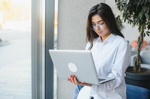 schöne kaukasische frau, die von etwas träumt, während sie mit einem tragbaren netbook in einer modernen cafébar sitzt, junge charmante freiberuflerin, die während der arbeit am laptop über neue ideen nachdenkt foto