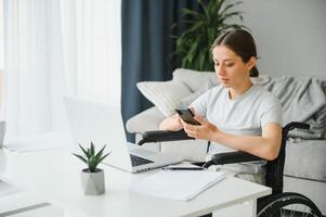 Frau im ein Rollstuhl funktioniert auf das Laptop pc im das Zuhause Büro mit ein Hilfe Hund wie ein Begleiter foto