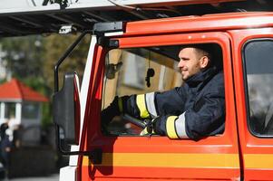 Porträt von glücklich jung Feuerwehrmann Fahren Feuerwehrauto beim Bahnhof foto