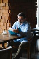 reifen gut aussehend Mann lesen ein Buch im ein Cafe foto