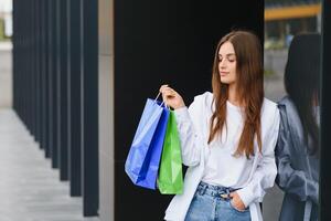 schön jung Frau mit Einkaufen Taschen in der Nähe von Geschäft draußen. foto