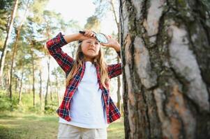 Bild von süß Kind mit Vergrößerung Glas erkunden das Natur draußen. bezaubernd wenig Mädchen spielen im das Wald mit Vergrößerung Glas. neugierig Kind suchen durch Lupe auf ein sonnig Tag im Park. foto