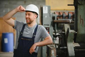 lächelnd und glücklich Mitarbeiter. industriell Arbeiter drinnen im Fabrik. jung Techniker mit Weiß schwer Hut. foto