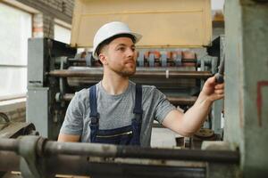 lächelnd und glücklich Mitarbeiter. industriell Arbeiter drinnen im Fabrik. jung Techniker mit Weiß schwer Hut. foto