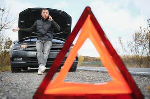 Mann reparieren ein gebrochen Auto durch das Straße. Mann haben Ärger mit seine gebrochen Auto auf das Autobahn Straßenrand. Mann suchen unter das Auto Haube. Auto geht kaputt Nieder auf das Autobahn. Straßenrand Hilfe Konzept. foto