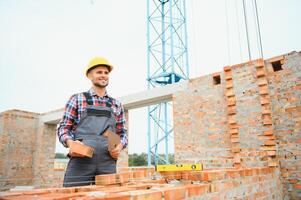 Konstruktion Arbeiter Mann im Arbeit Kleider und ein Konstruktion Helm. Porträt von positiv männlich Baumeister im Helm Arbeiten beim Konstruktion Seite? ˅. foto