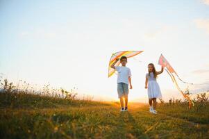 Bruder und Schwester spielen mit Drachen und Flugzeug beim das Feld auf das Sonnenuntergang. foto