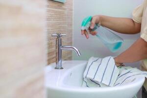 Hände von das Frau Verwendet Stoff und Wasser sprühen zu sauber das Bad sinken foto