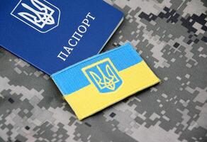 ukrainisch Reisepass und Flagge mit das Mantel von Waffen von Ukraine auf das Hintergrund von Militär- Tarnung. foto