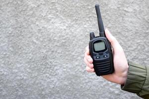 das Kerl ist halten ein Walkie-Talkie im seine Hand auf ein grau Hintergrund. foto