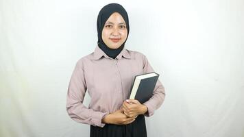 lächelnd jung asiatisch Muslim Schüler halten Buch, suchen beim Kamera isoliert auf Weiß Hintergrund. foto